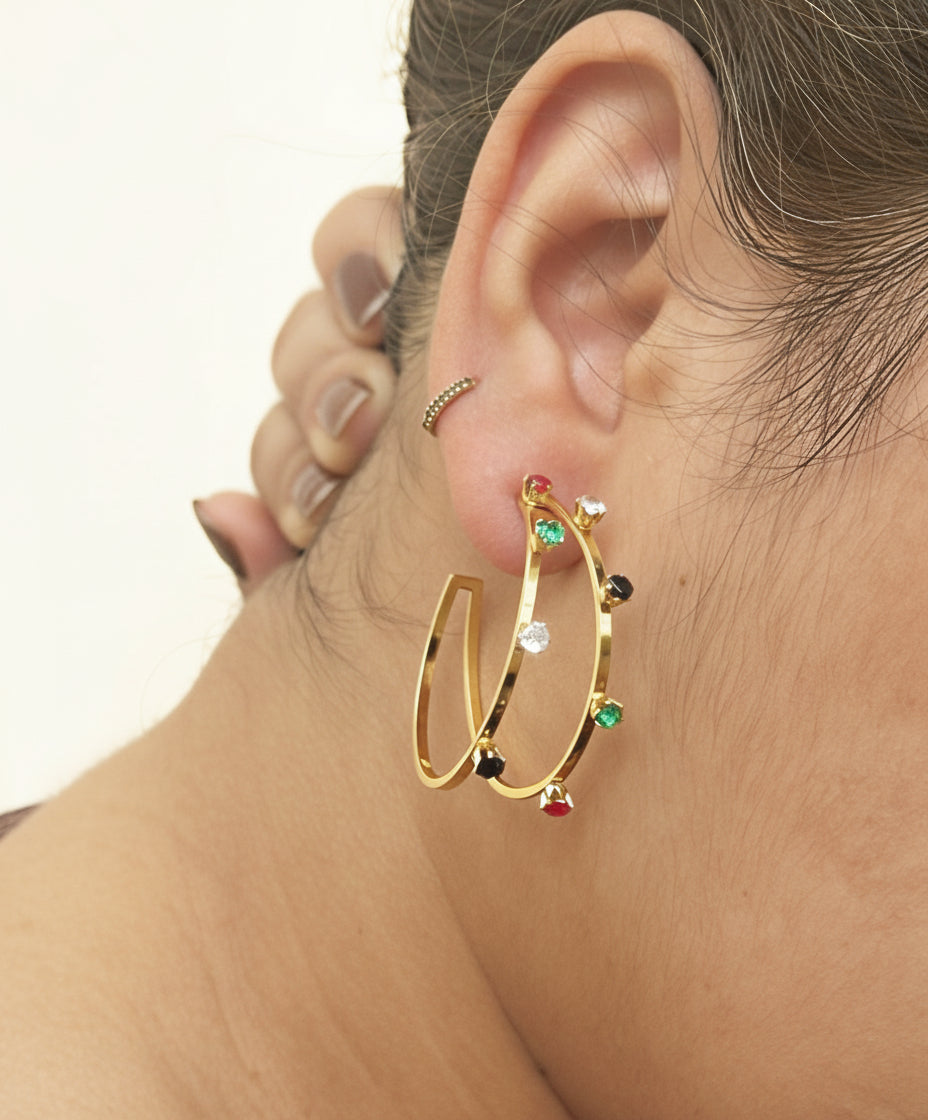 Gold hoop earrings with colorful gemstones worn by a person.