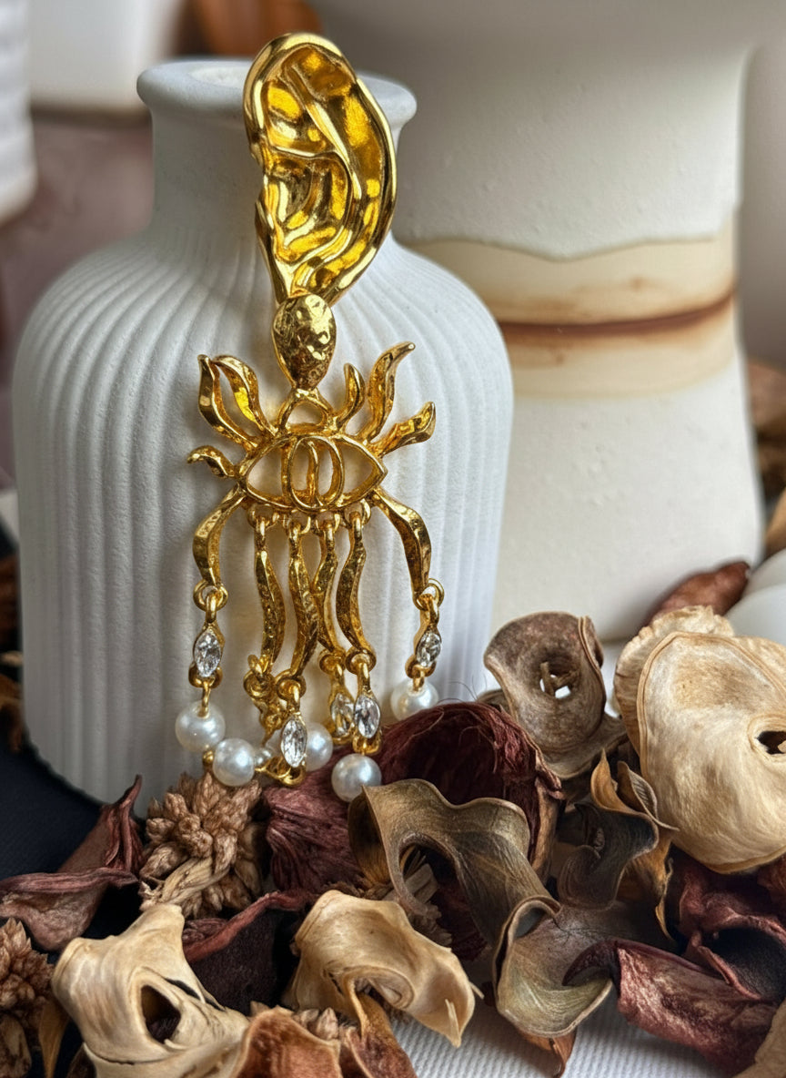 Gold earring with pearls on a decorative surface with dried flowers and a white vase.